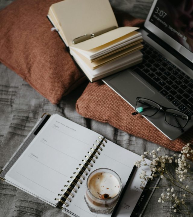 Black and Silver Laptop Computer Beside White Notebook and Black Framed Eyeglasses