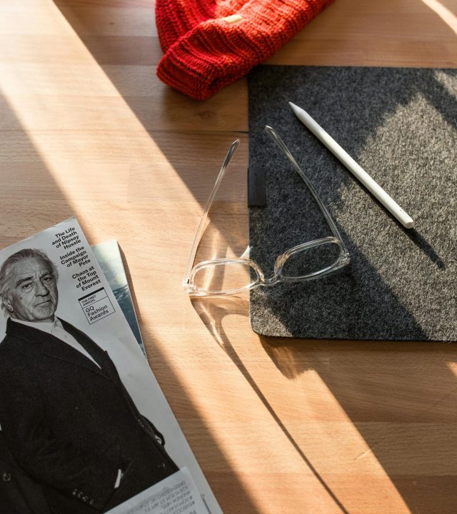 Stylish workspace featuring a red beanie, glasses, and a magazine in natural light.